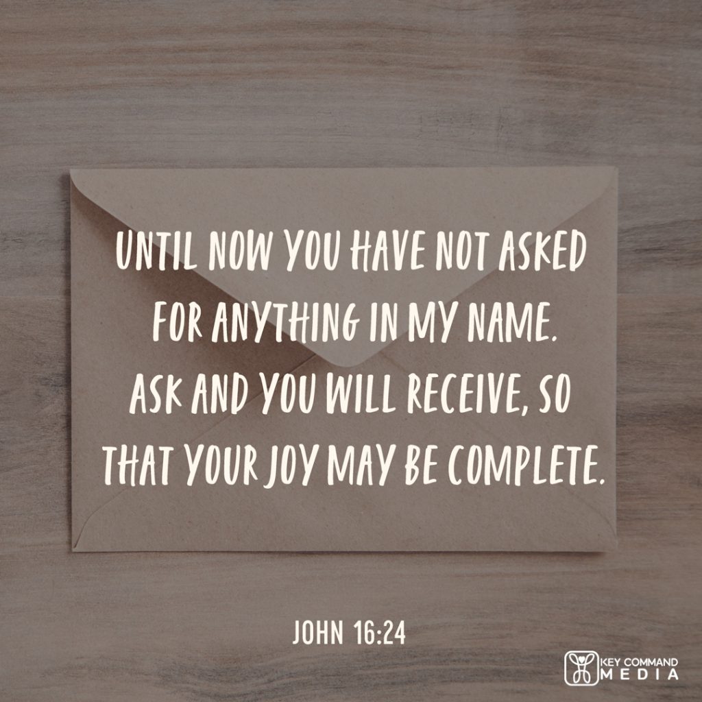 A tan, open envelope sits on a wooden desk with John 16:24, "Until now you have not asked for anything in My name. Ask and you will receive, so that your joy may be complete."