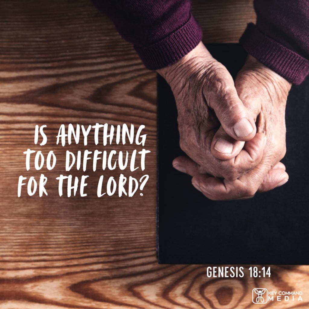 An overhead view of elderly hands folded on top of a Bible on a table with Genesis 18:14, "Is anything too difficult for the Lord?"