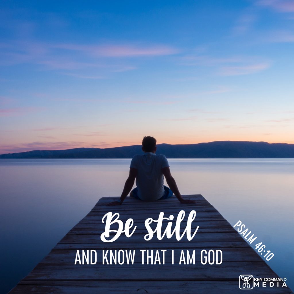 A lone man sits at the end of a dock overlooking a lake as the sun sets with Psalm 46:10, "Be still and know that I am God."
