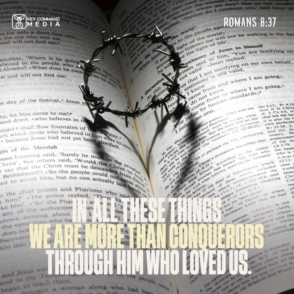 A small crown of thorns stands on the pages of an open Bible with Romans 8:37, "In all these things we are more than conquerors through Him who loved us."
