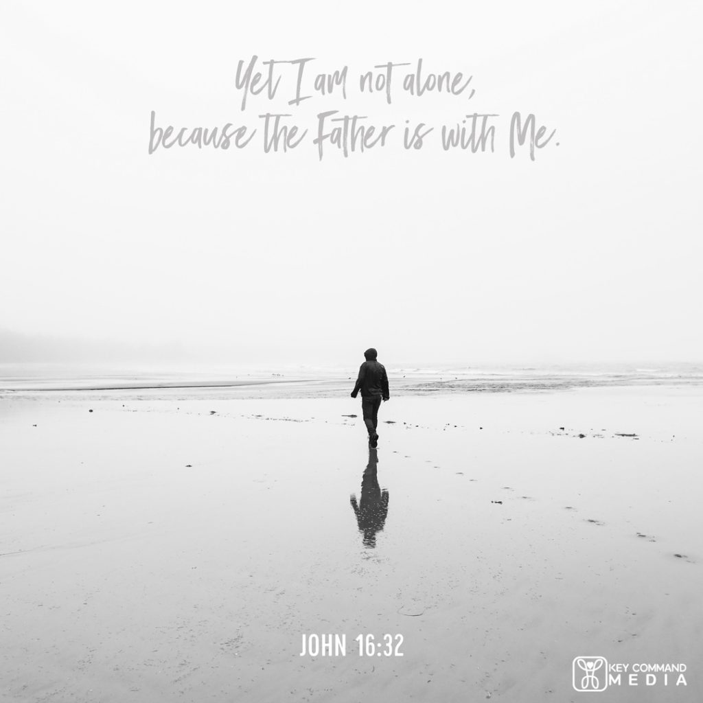 A black and white photo of a man walking alone along an empty shoreline on a cold, rainy day with John 16:32, "Yet I am not alone, because the Father is with me."