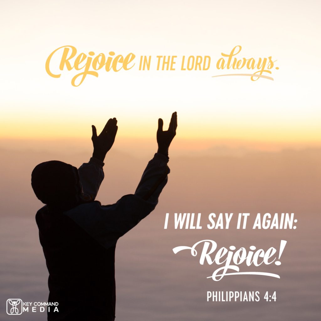 A man raises arms in silhouette as the sun rises over the mountain range in the distance with Philippians 4:4, "I will say it again: Rejoice!"